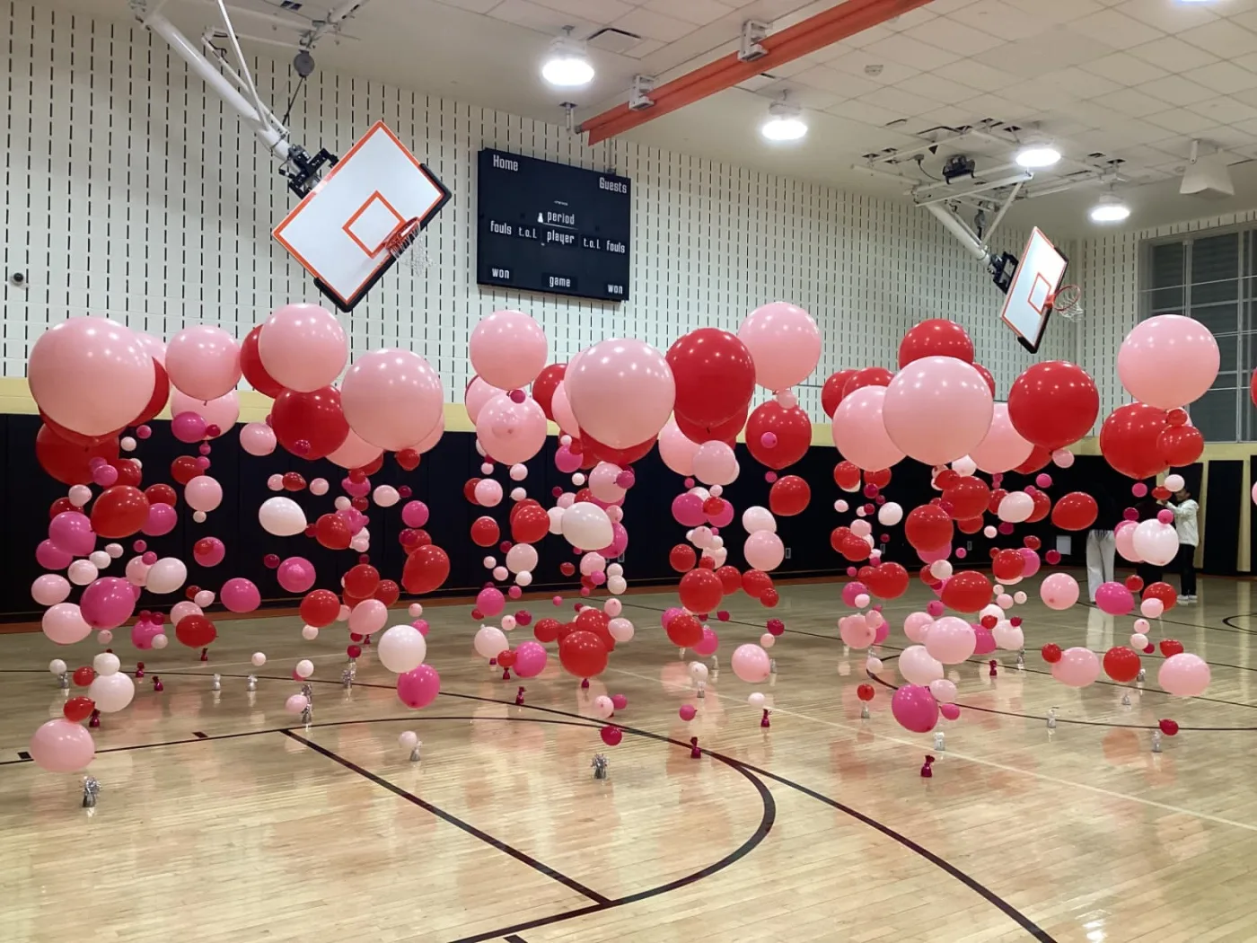 Rows of floating balloon columns with jumbo pink and red balloons and cascading strands filling a school gym, New Jersey