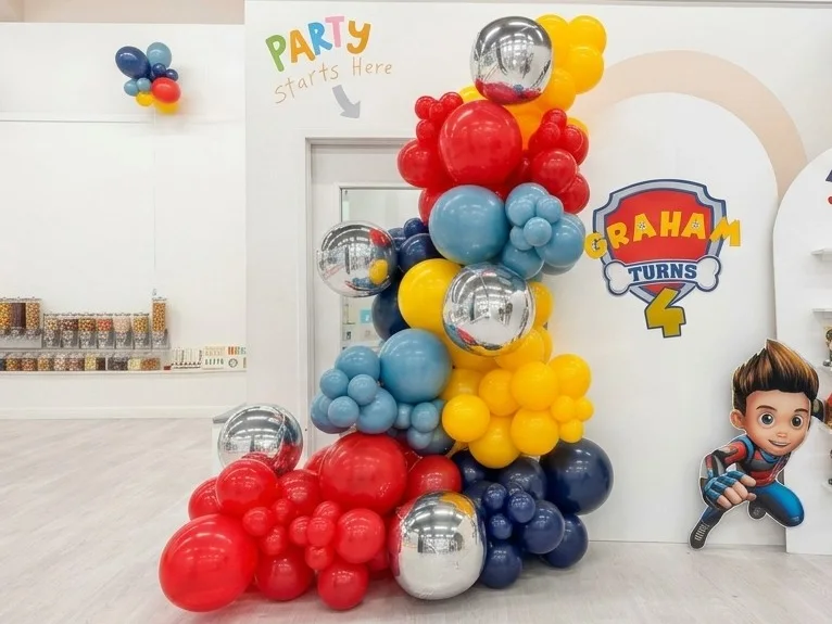 Organic balloon garland in red, yellow, blue and silver rising beside a doorway at a kids birthday party, New Jersey