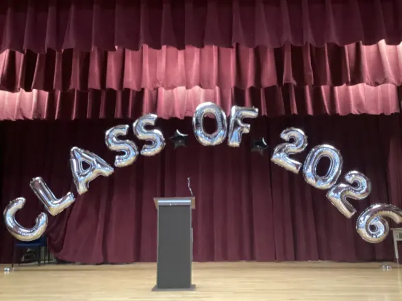 Silver CLASS OF 2026 foil letter arch over a school stage and podium, New Jersey