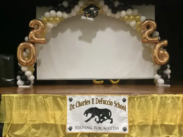 Black, white and gold balloon arch with gold 2026 foil numbers framing a school stage, New Jersey
