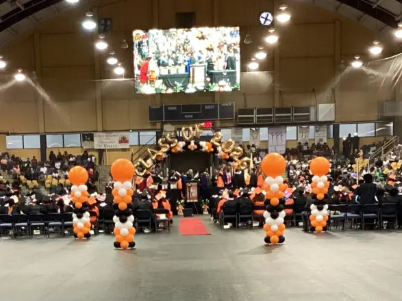 Orange and white balloon columns and a Class of 2026 balloon arch at an arena graduation ceremony, New Jersey