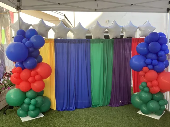Organic blue, red and green balloon columns with silver star foils framing a rainbow drape backdrop, New Jersey